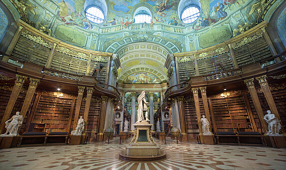 Hoher Saal unter einer barocken Kuppeldecke mit Statuen und Bücherregalen