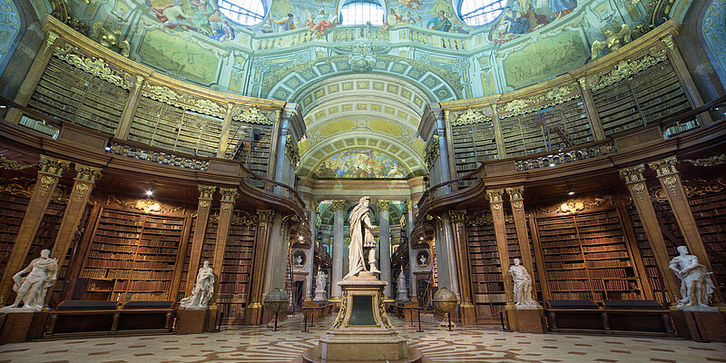 Hoher Saal unter einer barocken Kuppeldecke mit Statuen und Bücherregalen