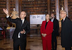 Ein Person führt zwei weitere durch einen Museumsraum.