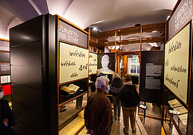 BesucherInnen im Literaturmuseum neben Bücherregalen mit großen Schautafeln.