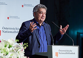 Person im Anzug am Rednerpult. 