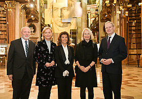 Fünf Personen in eleganter Kleidung posieren vor dem goldenen Porträt von Beethoven im Prunksaal.