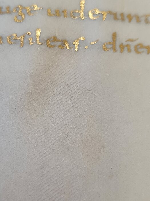 Nachaufnahme von Pergament mit Goldschrift, auf dem feine, gleichmäßige Linien zu sehen sind.