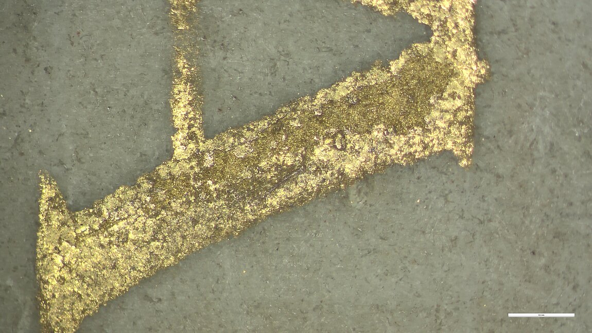 Detailaufnahme von Goldschrift, in der die Struktur des Pergaments genau erkennbar ist.