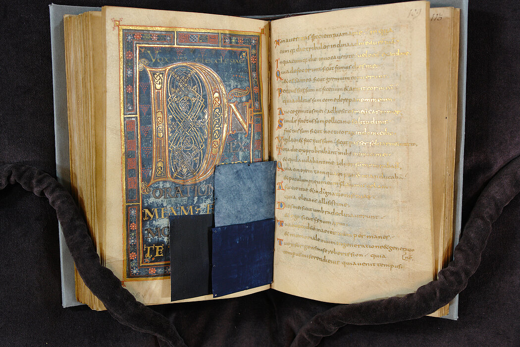 Doppelseite eines reichhaltig in Gold, Blau und Rot verzierten Buchs, links ist der untere Teil der Seite teils von blauem Material bedeckt.