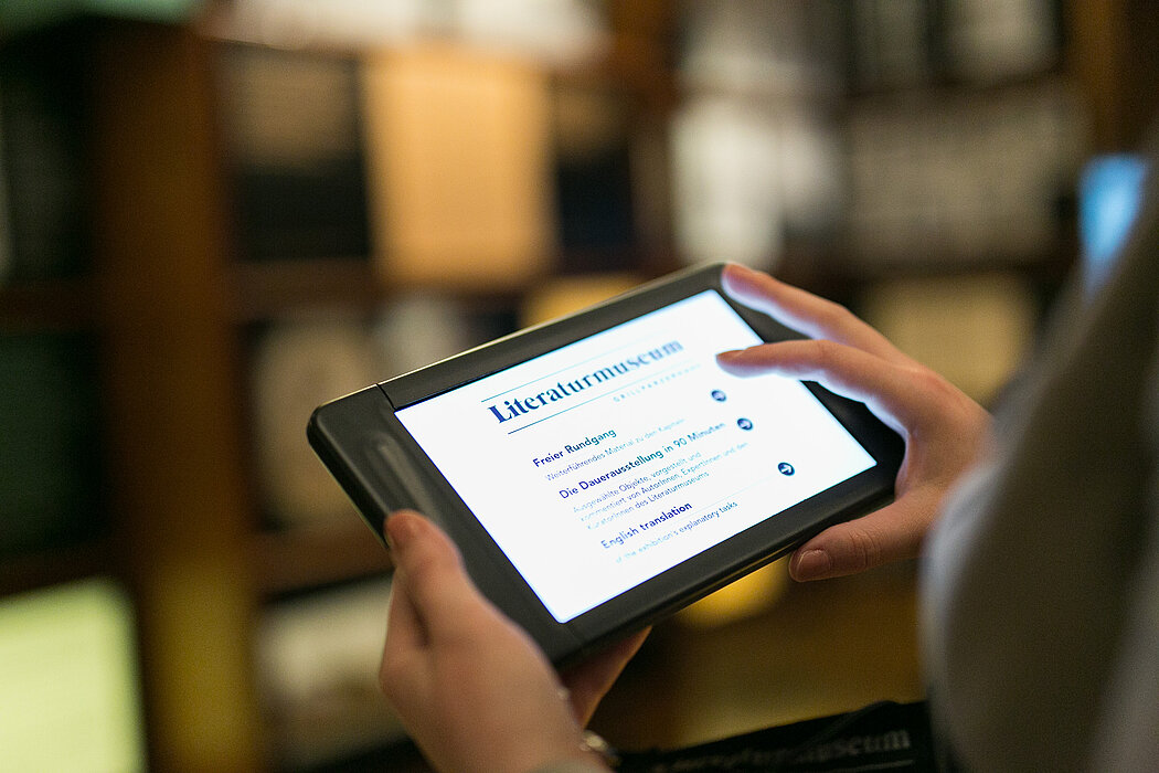 Zwei Hände halten Museumstablet des Literaturmuseums der ÖNB, Bedienung durch Touchpad