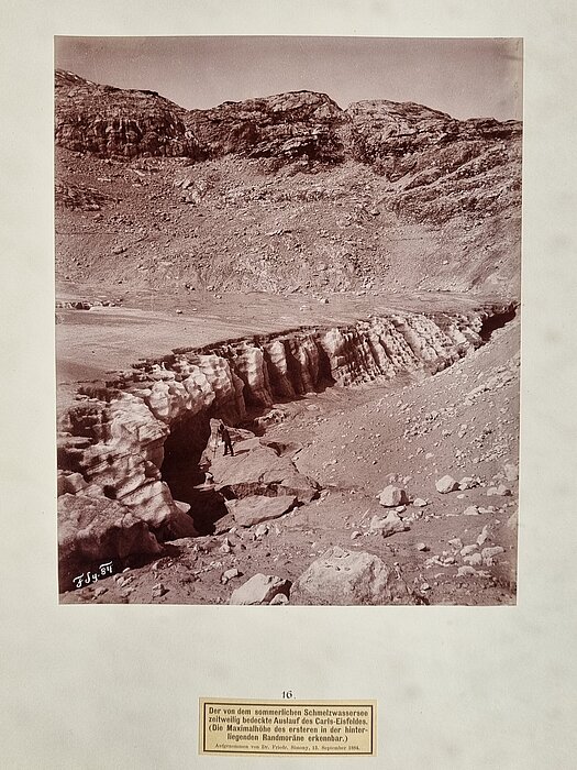 Klippe eines Gletschers, davor steht eine Person mit einem Stativ.