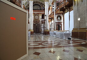 Holzkiste links lenkt den Blick auf die Leiter hinten im Saal.