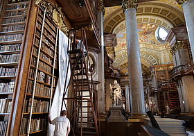 Zwei Personen befestigen weißes Papier an einem hohen Bücherregal.