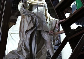 Person reinigt eine weiße Statue mit Schwamm.