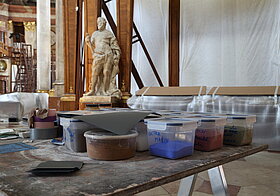 Pulverfarben in kleinen Plastikboxen stehen auf dem Tisch.