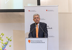 Person in Anzug an Pult auf Bühne.