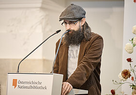 Mann steht vor einem Podium und hält eine Rede. 