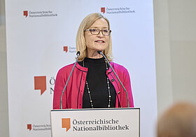 Frau steht vor einem Podium und hält eine Rede. 