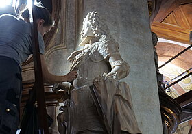 Person reinigt eine weiße Statue mit Schwamm.