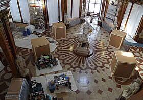 Statue in der Mitte des Saales, rundherum große Holzkisten.