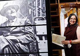 Andrea_Mayer.jpg Person steht lächelnd im Literaturmuseum. Links im Vordergrund ein Foto von Stefan Zweig.