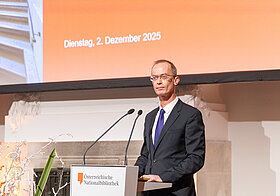 Eine elegant gekleidete Person spricht an einem Rednerpult.