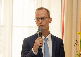 Elegant gekleidete Person spricht mit einem Mikrofon.