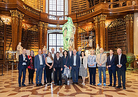 Gruppe von Menschen posiert in Marmorsaal mit Bücherregalen und grün beleuchteter Statue.
