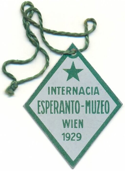 Abzeichen des Internationalen Esperanto-Museums in Wien anlässlich seiner Eingliederung in die Nationalbibliothek. Blech, mit grünem Aufdruck, an grüner Schnur hängend