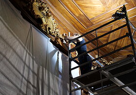 Person mit Pinsel an einem gold verzierten Bücherregal