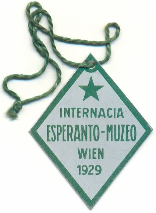 Abzeichen des Internationalen Esperanto-Museums in Wien anlässlich seiner Eingliederung in die Nationalbibliothek. Blech, mit grünem Aufdruck, an grüner Schnur hängend