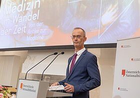Richard_Starkel.jpg Eine Person steht auf einem Podium vor einem Mikrofon und spricht.