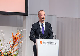 Richard_Starkel_2.jpg Eine elegant gekleidete Person spricht an einem Rednerpult.