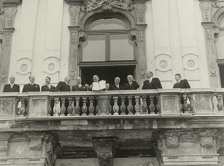 Abb1.jpg Schwarz-Weiß Foto eines alten Gebäudes mit einen Balkon mit vielen Menschen.
