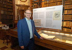 Marko_Deisinger_2.jpg Elegant gekleidete Person vor einer Vitrine in einer alten Bibliothek.