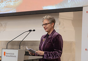 Michaela_Mayr.jpg Eine Person steht auf einem Podium und spricht in ein Mikrophon