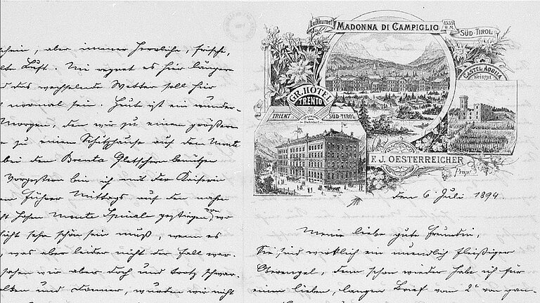 Kurrent.jpg Schwarz-weißes Bild einer handschriftlichen Seite in Kurrentschrift, links dichter Text, rechts eine Illustration mit Landschaftsansicht von Madonna di Campiglio in Südtirol, einem Hotelgebäude und einer Burg, umgeben von dekorativen Pflanzenmotiven. Darunter ein Datum: 6. Juli 1894.
